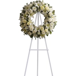 White floral wreath of lilies, roses, carnations, and mums on a tall white easel stand