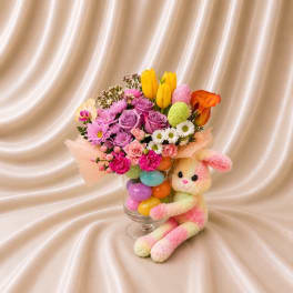 Colorful bouquet in a glass vase with a plush bunny beside it
