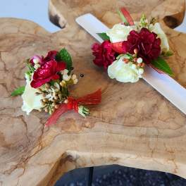 Two floral boutonnieres with red and white blooms on a wooden surface