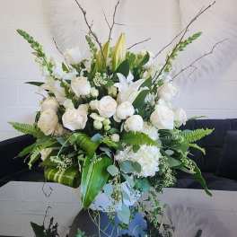 Large white flower arrangement with roses, lilies, and snapdragons in a white vase with lush greenery.