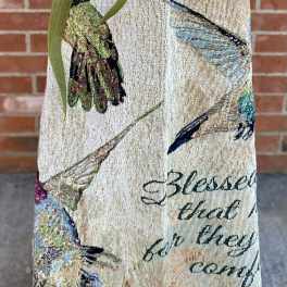 Decorative hanging textile with a green bow against a brick wall