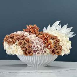 Low floral arrangement of roses and orchids in a white vase