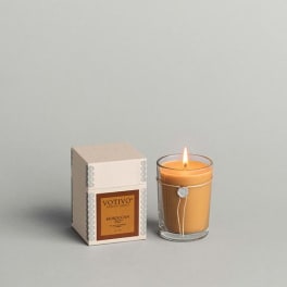 Lit amber candle in a glass holder beside its box