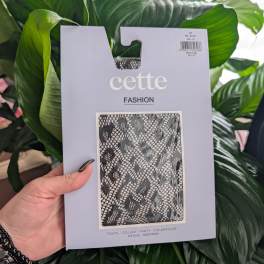 Packaged black patterned tights held in front of large green leaves