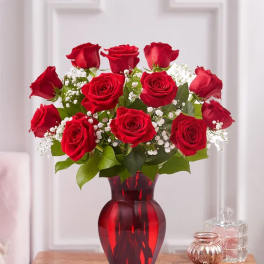 Red roses arranged in a red glass vase with baby's breath
