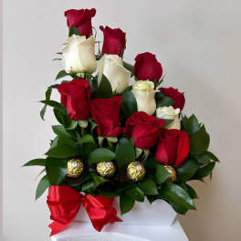 Red and white roses arranged with chocolates and a red ribbon