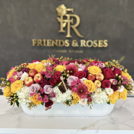 Large mixed flower arrangement in a white rectangular container with apples