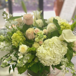 Mixed bouquet of pale roses, hydrangeas, and white calla lilies in a glass vase
