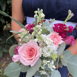 Hand-tied bouquet of pink roses, carnations, and white blooms with eucalyptus, held against a navy dress.