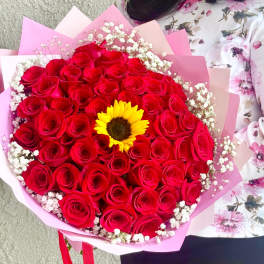 Bouquet of red roses with a yellow sunflower center and pink wrapping