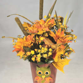 Orange floral arrangement in a painted owl pot with autumn leaves