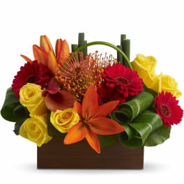 Low rectangular arrangement of yellow roses, red gerberas, and orange lilies in a wooden container