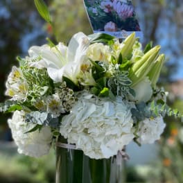 White floral arrangement in a glass vase with lilies and hydrangeas