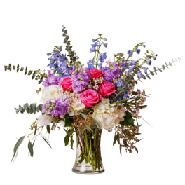 Bouquet of pink roses, purple flowers, and white blooms in a clear glass vase