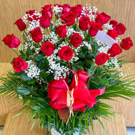 Red roses arranged in a white basket with baby's breath and a red bow