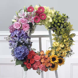Colorful open floral wreath in a rainbow gradient displayed on a white easel.