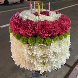 Round floral cake with pink, white, and green flowers and striped candles
