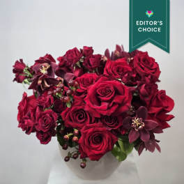 Deep red roses and orchids arranged in a white vase