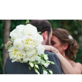 White bridal bouquet with trailing blooms held by a couple embracing