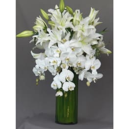 White lilies and orchids arranged in a tall green vase