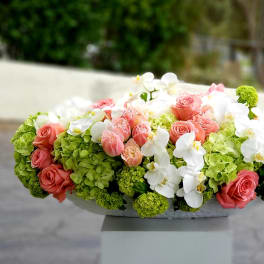 Pink roses and white orchids arranged with green hydrangeas in a low container