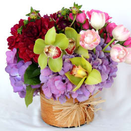 Mixed bouquet with orchids, hydrangeas, and tulips in a woven basket