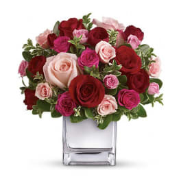 Bouquet of red, pink, and blush roses in a clear square vase
