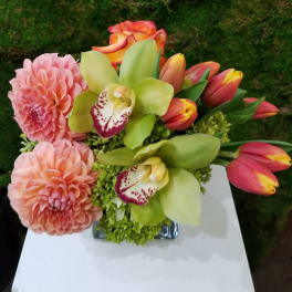 Pink dahlias, green orchids, and tulips in a glass vase