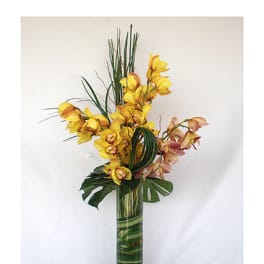 Tall arrangement of yellow and pink orchids in a green glass vase