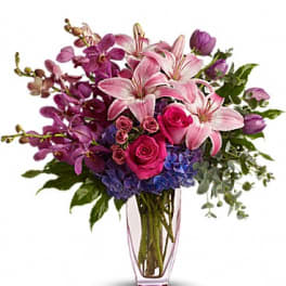 Pink lilies, roses, and purple orchids arranged in a clear vase.