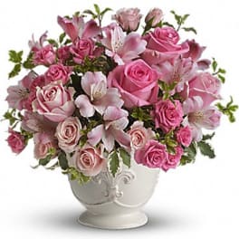 Pink roses and lilies arranged in a white urn vase