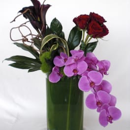 Arrangement of red roses, purple orchids, and dark calla lilies in a green vase