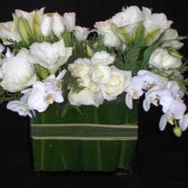 White floral arrangement with orchids and roses in a green vase