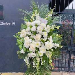 Tall white floral standing spray on an easel with palm fronds