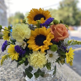 Mixed bouquet in a clear glass vase with sunflowers, a peach rose, and carnations