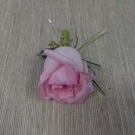 Pink rose boutonniere with decorative grass accents on a woven surface