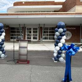 Blue and white balloon columns flank a podium outside a building.