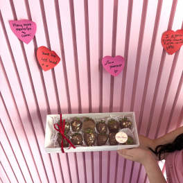 Box of chocolate-covered strawberries held in front of pink heart notes