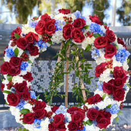 Large floral wreath of red roses, white blooms, and blue flowers on an easel