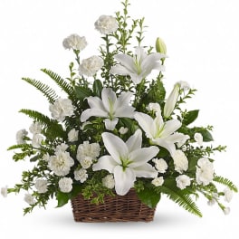 White lilies and carnations arranged in a wicker basket with lush greenery.