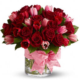 Bouquet of red roses and pink tulips in a glass vase with a pink ribbon