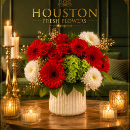 Red and white flower arrangement in a white vase with candles nearby