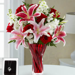 Red roses and pink lilies arranged in a red glass vase