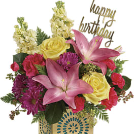 Mixed bouquet with pink lilies, yellow roses, and purple flowers in a gold vase