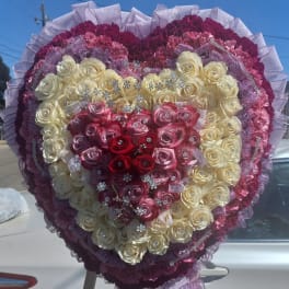 Heart-shaped rose arrangement in cream, pink, and red with purple ribbon trim
