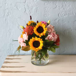 Sunflowers and pink flowers arranged in a clear glass vase