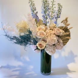 Tall floral arrangement with pale roses, hydrangeas, and blue delphinium in a green vase