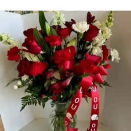Red and white floral bouquet in a glass vase with red ribbons