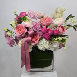 Pink and white floral arrangement in a clear square vase with a satin ribbon