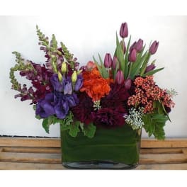 Purple and orange mixed flower arrangement in a green glass vase